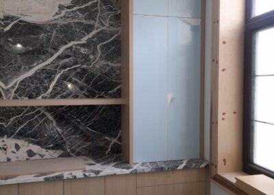 Oak base cabinets and a tall gloss cabinet beside a marble wall